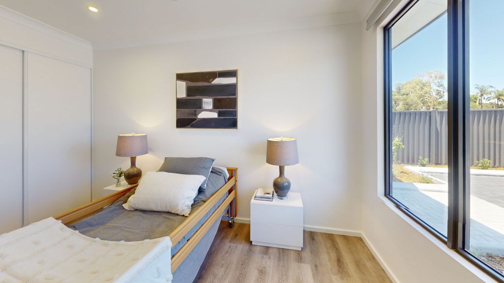 An interior image showing the bedroom of one of the homes at Grant Lewis Court in Gosnells. The bedroom is finished with automatic blinds, it's own accessible ensuite and can comfortably fit a double bed. The rooms also have ample built in wardrobes and storage.