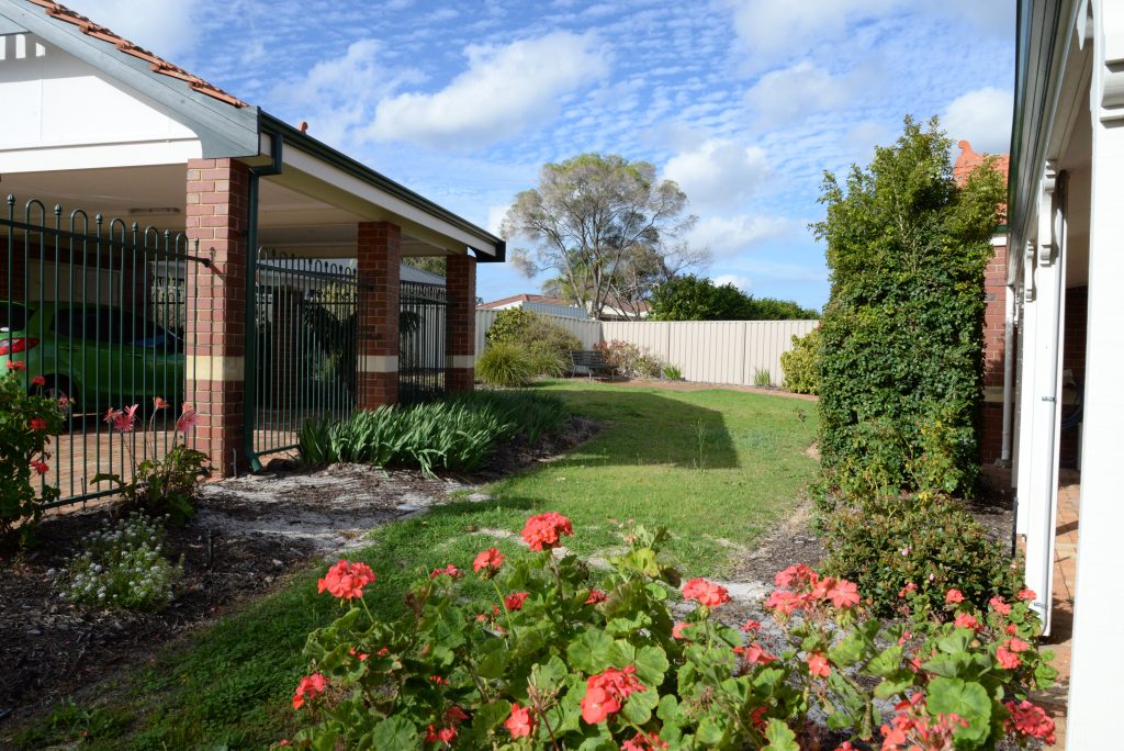 Side of red brick house and back garden with green grass and pink flowers